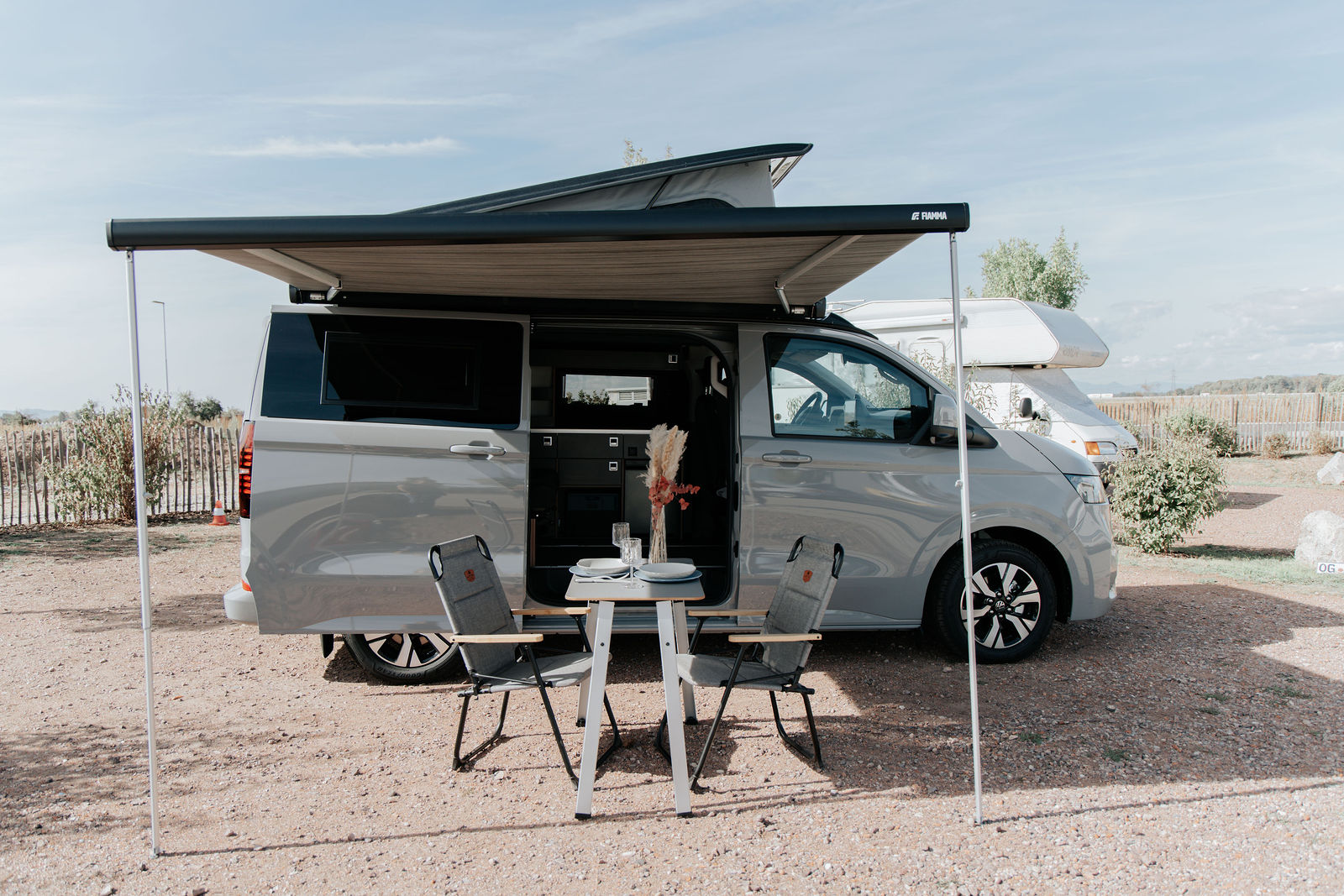 WSR Classic Campervan auf VW T7 Basis mit ausgefahrener Markise und gedecktem Tisch auf dem Campingplatz